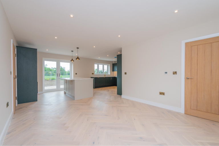 Open-plan living space with herringbone flooring, looking through to the kitchen beyond