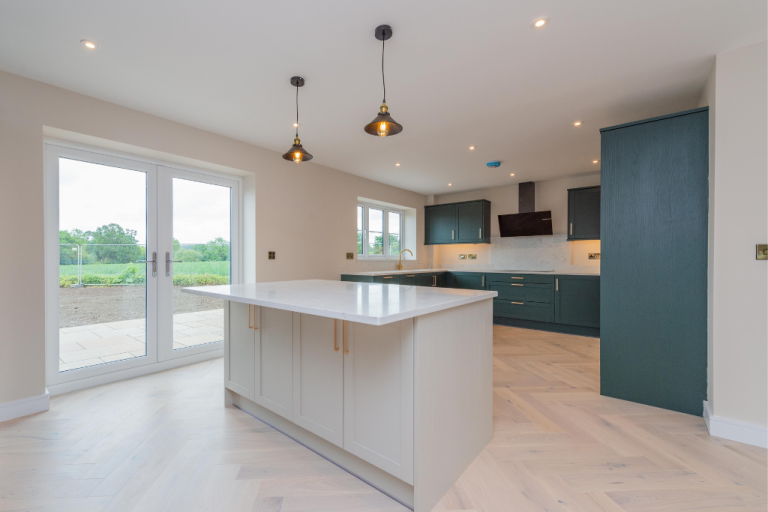 Open-plan kitchen with a central island, dark green units and bi-fold doors onto the garden