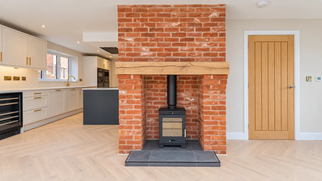 Open-plan kitchen with brick fireplace, The Farmyard at Grafton Open-plan kitchen and living space with an exposed brick fireplace, oak beam and wood burner at The Farmyard at Grafton